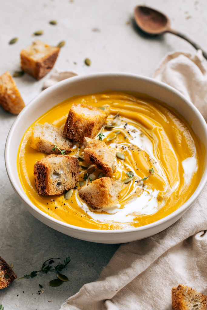 Close-up of creamy roasted vegan butternut squash soup with toasted croutons, coconut cream, pumpkin seeds, and fresh thyme.